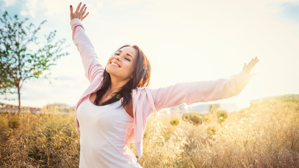 Woman laughing outdoors with arms raised towards the sky— feeling the positive energy of physical activity and movement.